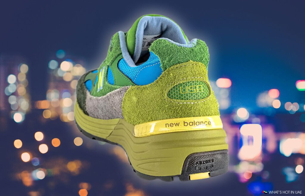 A colorful sneaker featuring green suede, a yellow sole, and "new balance" branding against a blurred cityscape background.