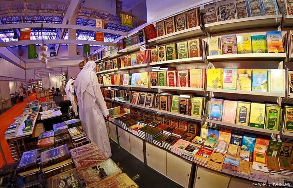 A man in traditional attire browses books on well-stocked shelves at a book fair.