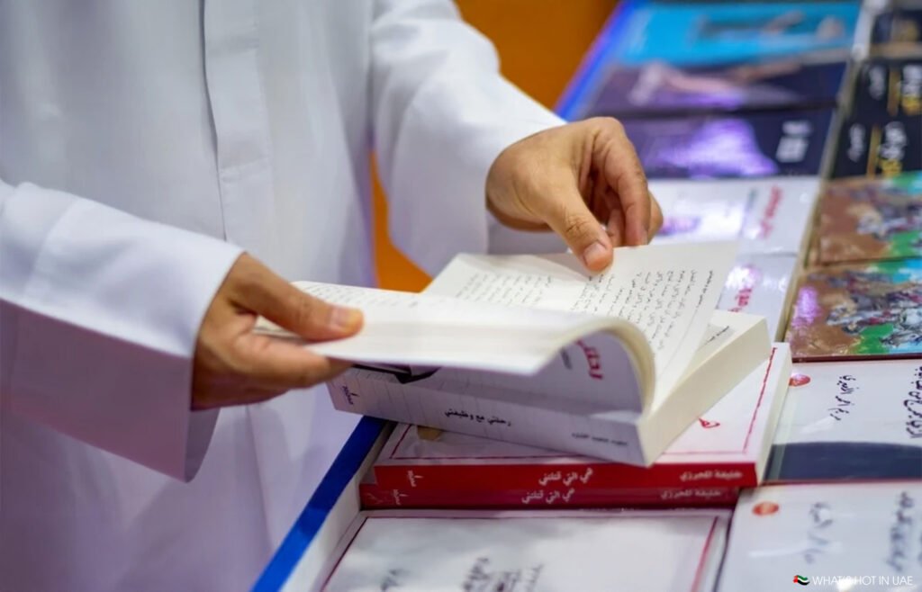 A person in a white garment flips through a book at a table with several other books.