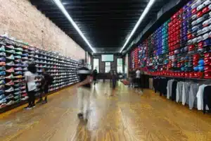 People browsing sneakers and hats on display in a store with brick walls and wooden flooring.