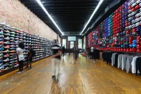 People browsing sneakers and hats on display in a store with brick walls and wooden flooring.