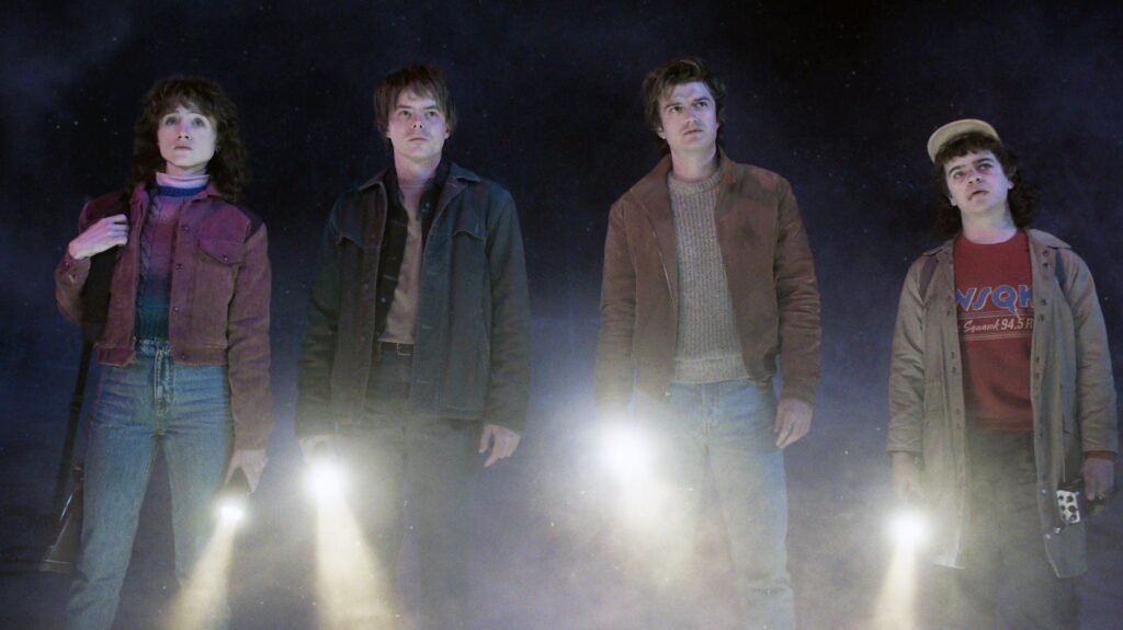 Four main characters from Stranger things 5 standing with torches in a dark environment