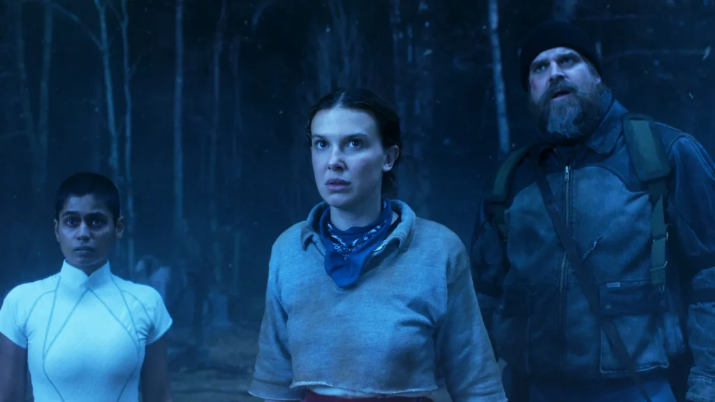 Three characters from Stranger things 5 in a dark area of a wooded area