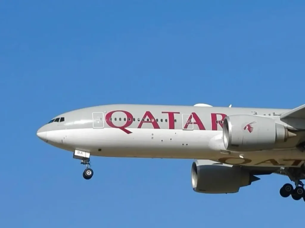 Qatar Airways aircraft captured mid-flight against a clear blue sky, highlighting the airline’s fuselage branding.