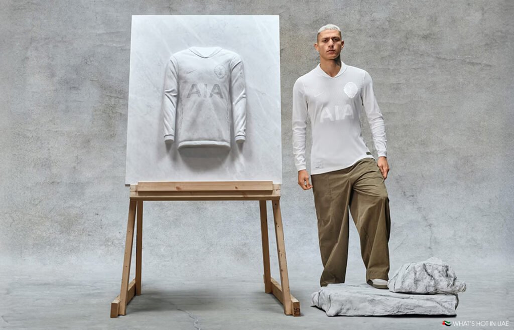 A man in casual pants and a white shirt stands next to an easel displaying a sculpted jersey.