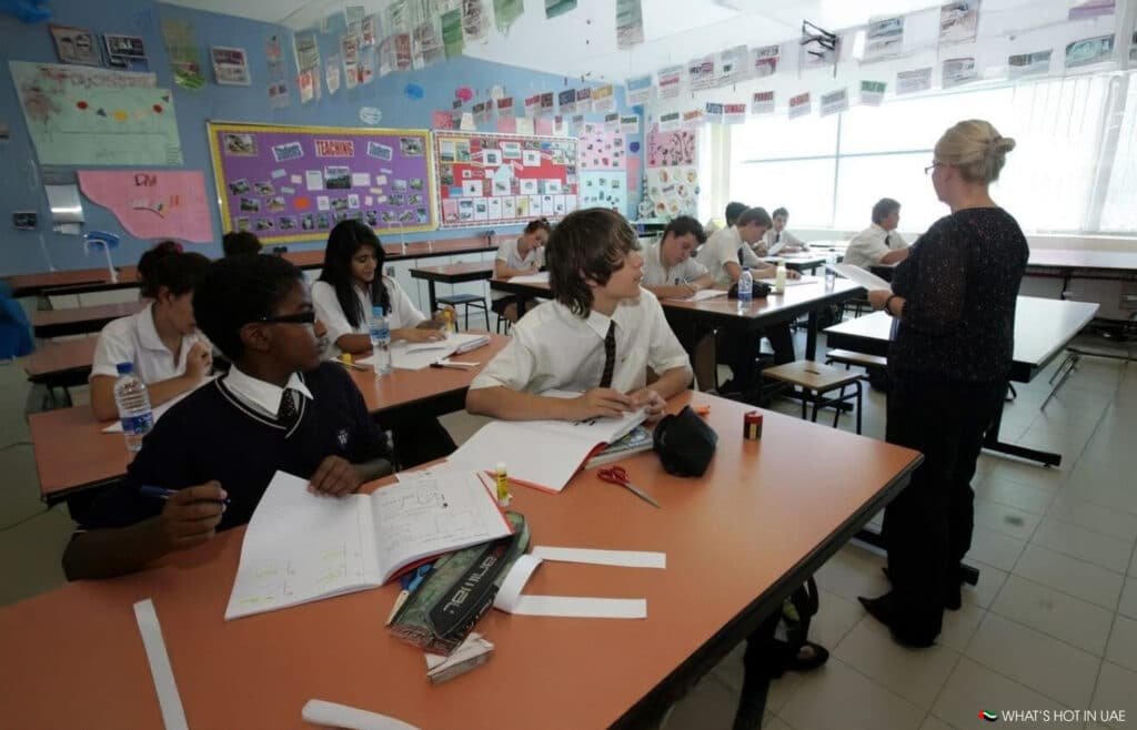 A UAE Schools classroom with students sitting at desks, working on assignments, while a teacher stands at the front teaching about AI.