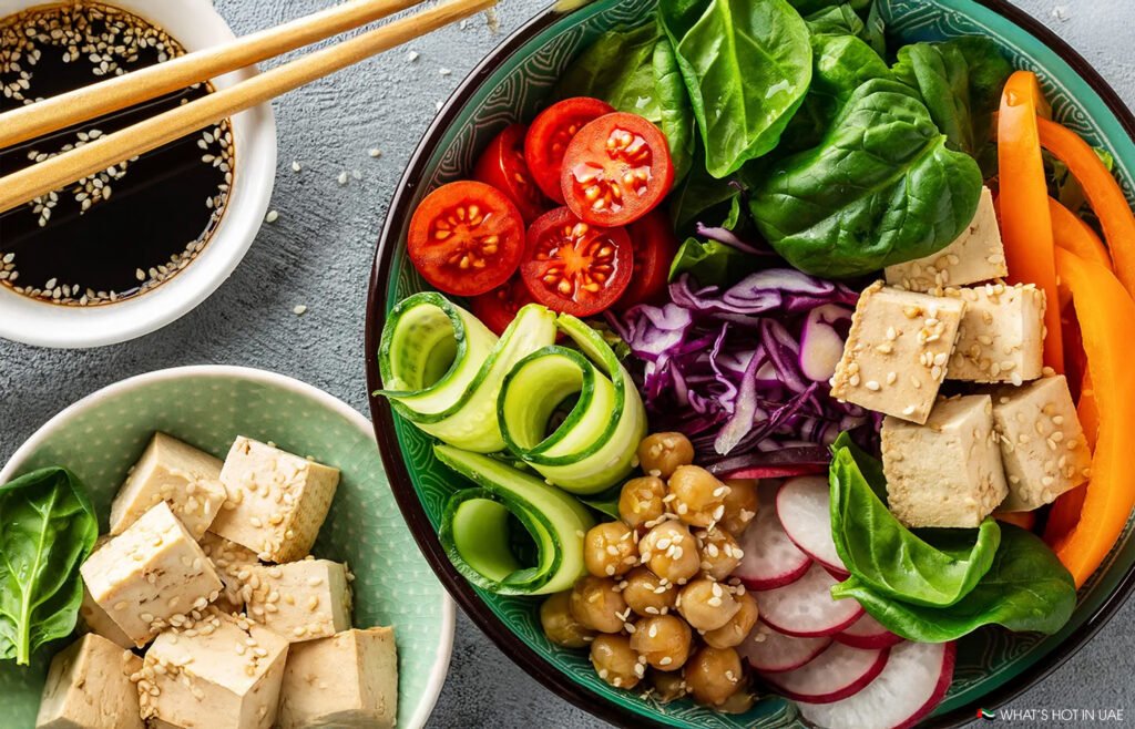 A colorful Veganuary in Dubai bowl with tofu, spinach, cherry tomatoes, cucumber, radishes, red cabbage, and chickpeas, next to a soy sauce dish.