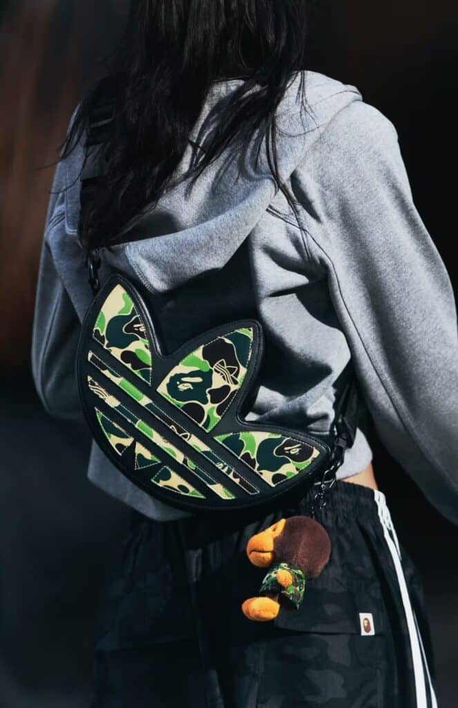 A person wearing a gray hoodie and camouflage bag with a plush toy attached.