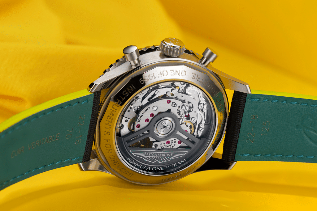 A Breitling Navitimer Aston Martin watch with a transparent back displaying its intricate mechanism and an Aston Martin inscription, set against a vibrant yellow background.
