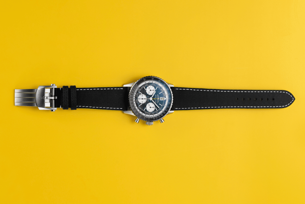 A wristwatch with a black leather strap and a silver buckle on a yellow background.