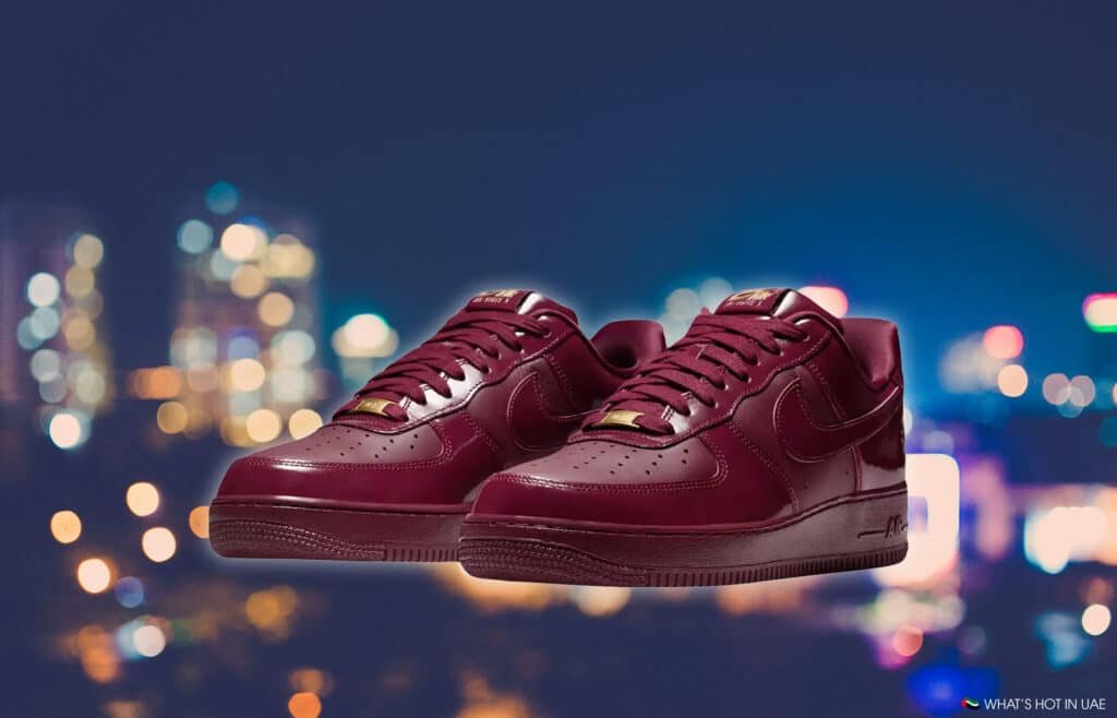 A pair of maroon sneakers with a glossy finish, displayed against a blurred city lights background.