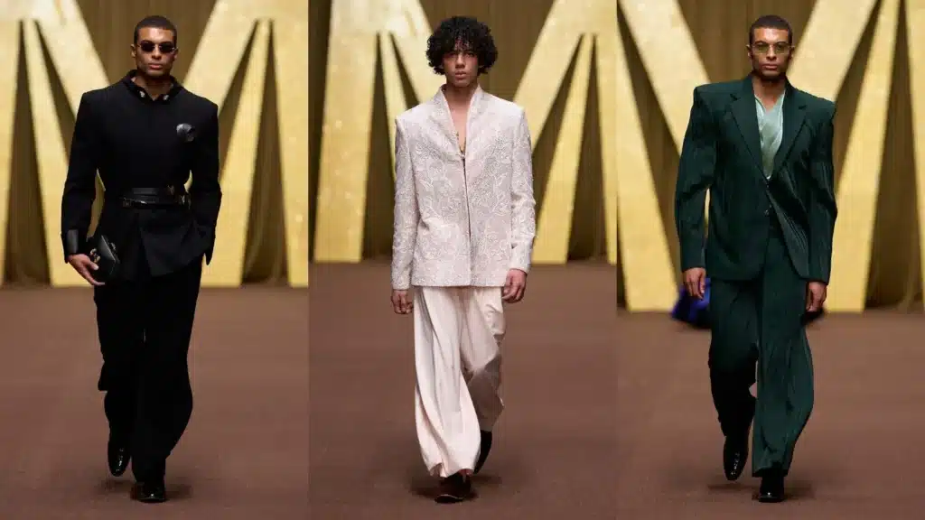 Three models walk the runway showcasing elegant suits in black, white, and green, with gold geometric background elements.