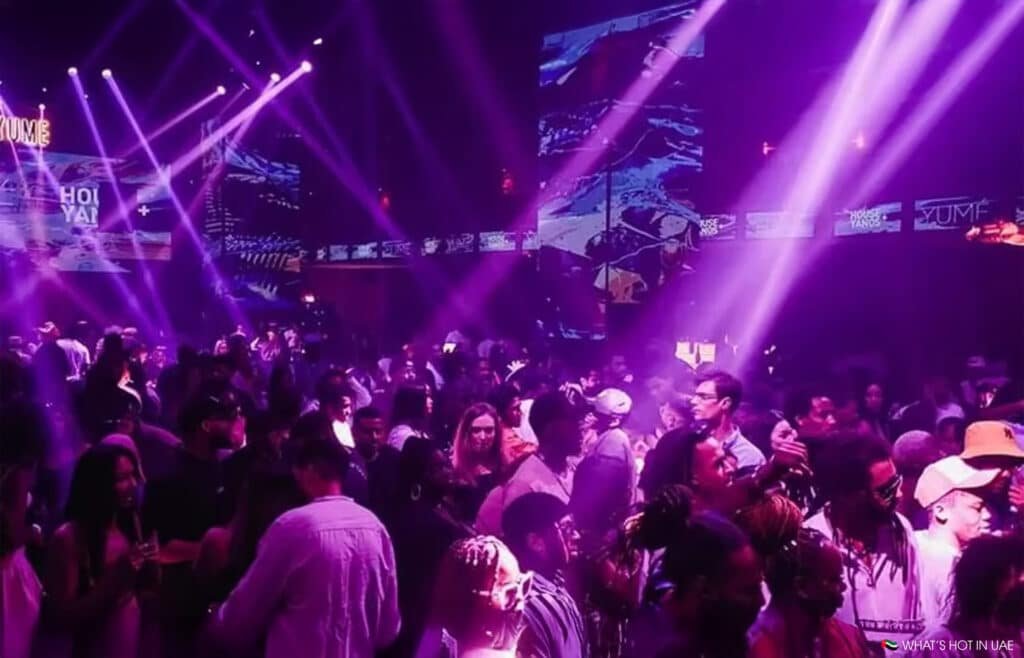 A crowded Dubai Nightlife nightclub with people dancing under purple and pink lights, surrounded by glowing screens and vibrant visuals.