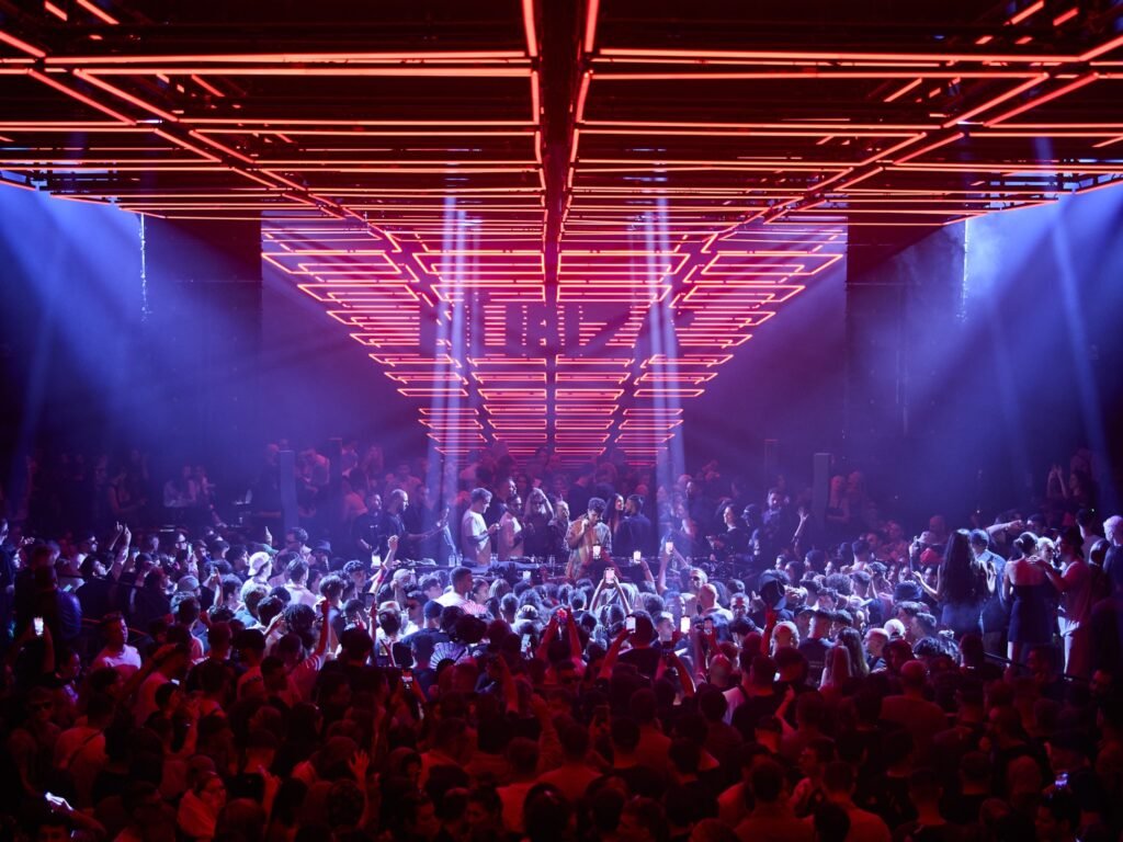 A crowded nightclub with vibrant red and blue lights illuminating the dance floor.