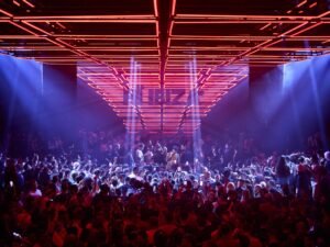 A crowded nightclub with vibrant red and blue lights illuminating the dance floor.