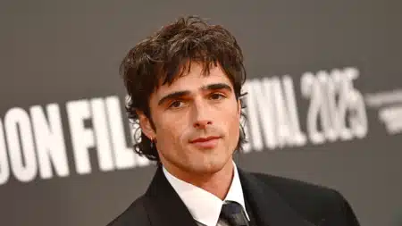 A person with medium-length dark hair, wearing a suit and tie, stands in front of a backdrop with the text "London Film Festival 2023."