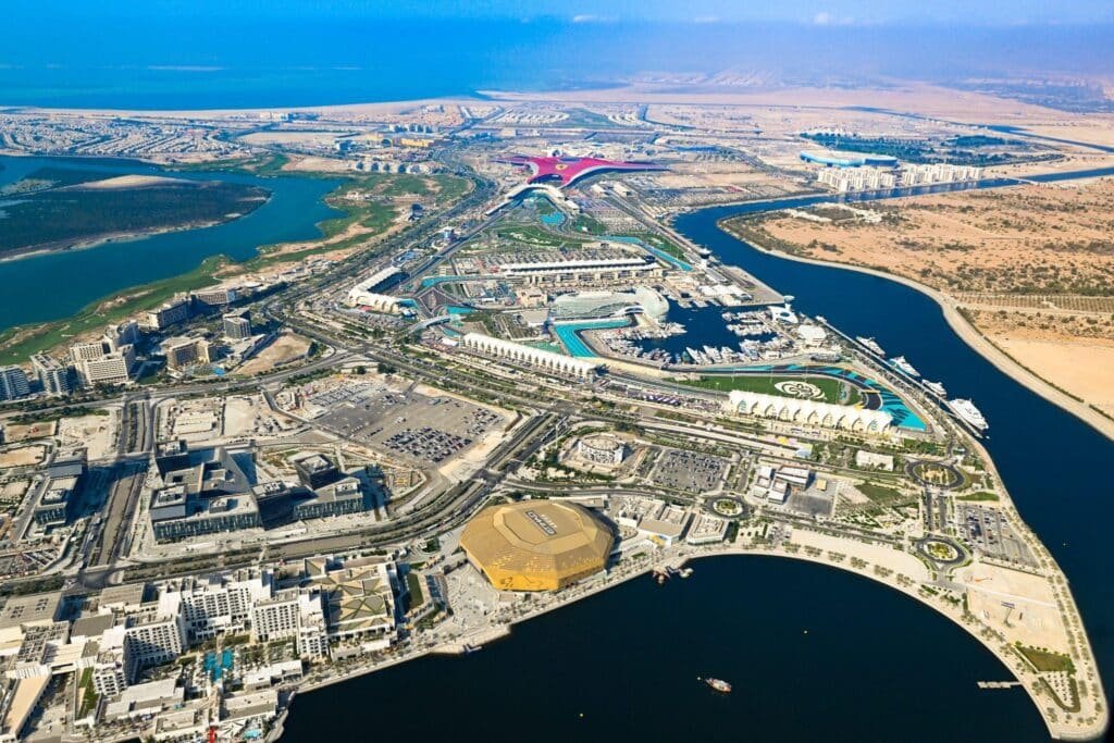 Aerial view of a large waterfront complex with a distinctive red-roofed building, surrounded by waterways and desert terrain.