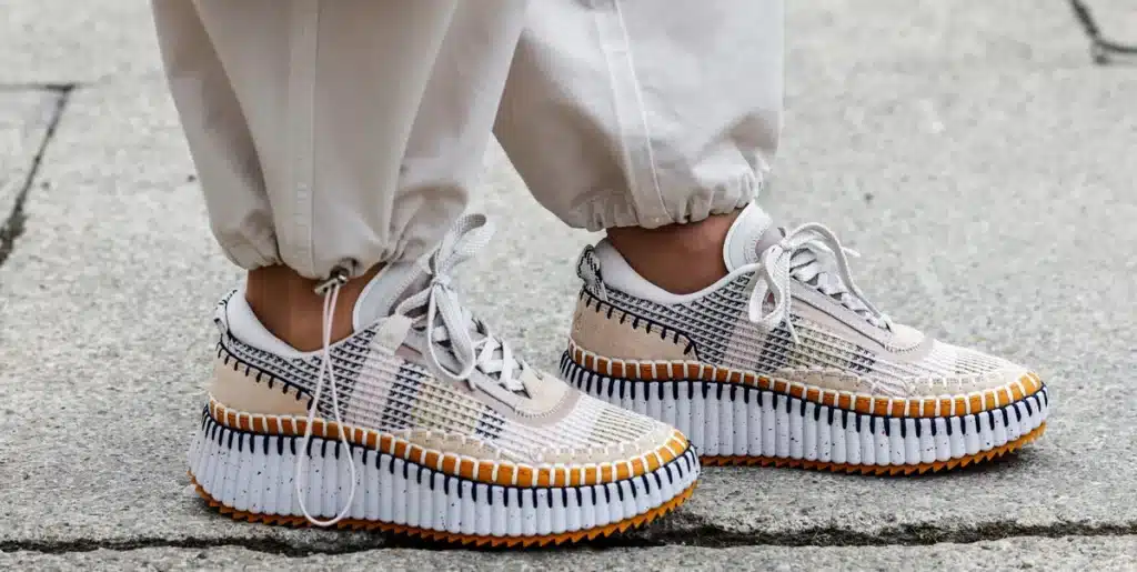 Person wearing stylish white and orange platform Luxury Sneakers with checkered pattern and white pants.