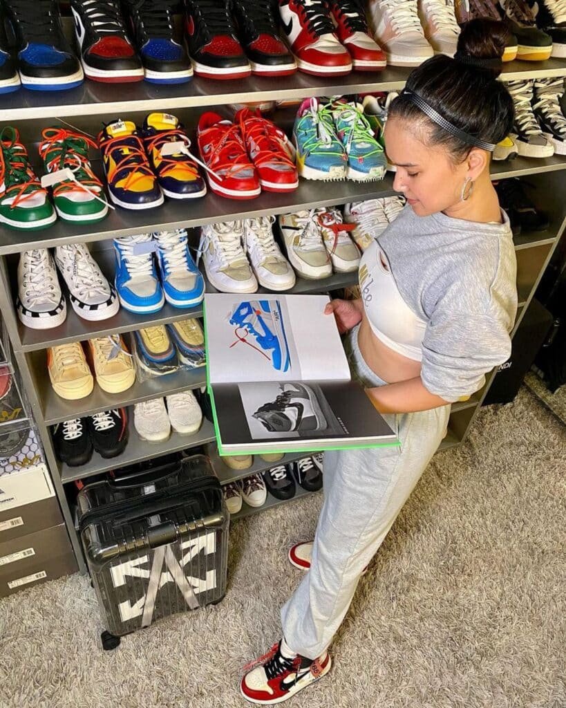 A person in casual attire stands in front of shelves filled with various Luxury Sneakers, holding a shoebox.