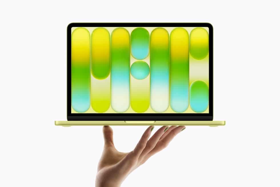 A hand holding a MacBook NEO laptop with a vibrant, abstract green and yellow pattern on the screen.