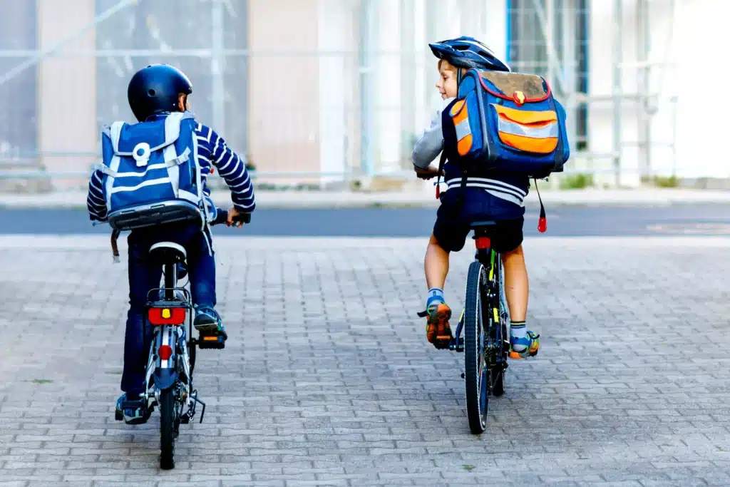 Minors on E-Bikes wearing helmets and backpacks on a paved street.
