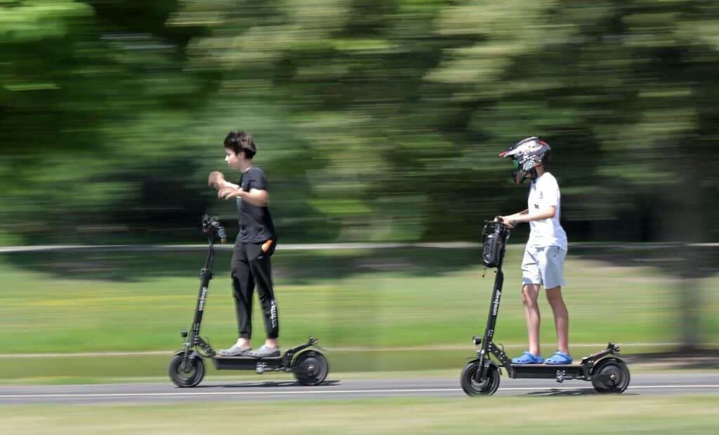 Minors on E-Bikes at high speed, one wearing a helmet, with blurred trees in the background.