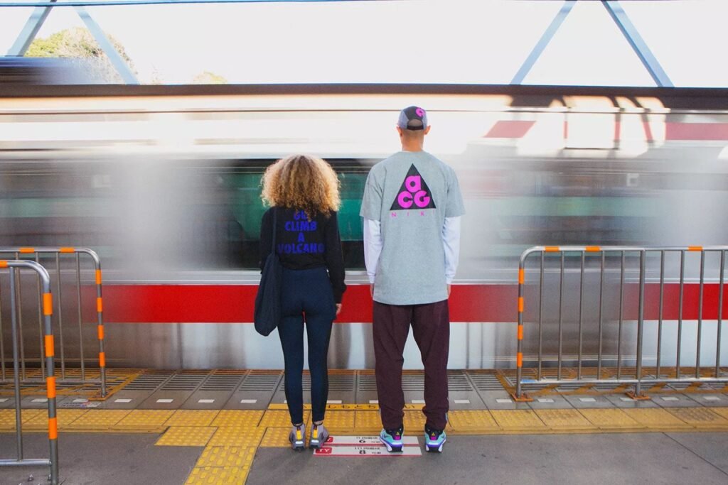 Two people stand at a train station platform with a speeding train passing by.