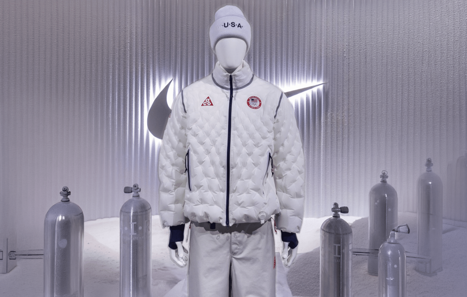 A mannequin wearing a USA Olympic outfit with a quilted white jacket and a beanie, surrounded by glass tanks and a large Nike logo.