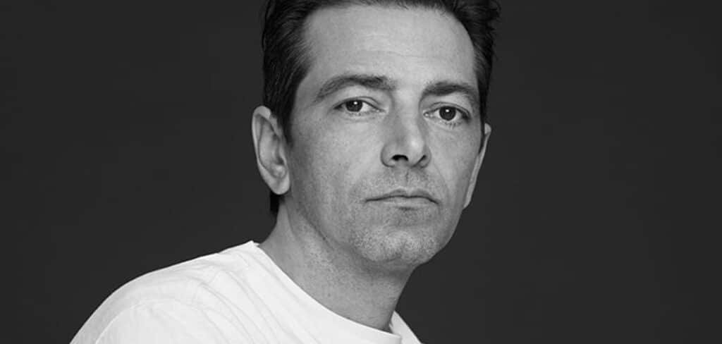 Pieter Mulier with short dark hair and a serious expression, wearing a white shirt, set against a dark background.