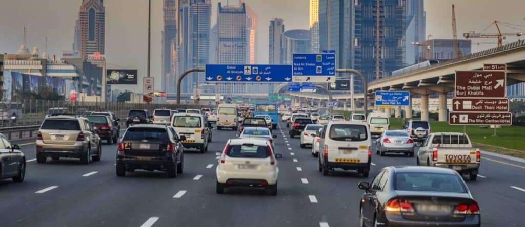 Ramadan Rush Hour Traffic on a multi-lane highway in an urban area with skyscrapers and directional signs in the background.