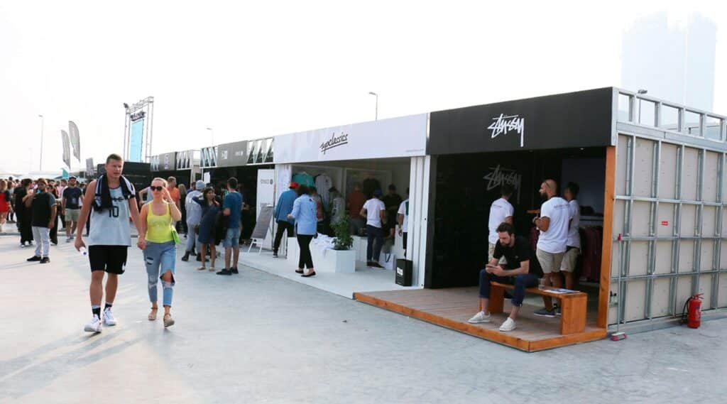 People walking and shopping at outdoor pop-up stores featuring clothing brands on a sunny day. Sneaker Culture in the UAE