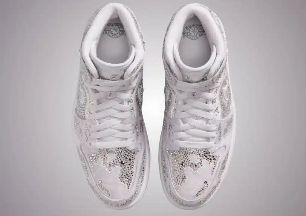 A pair of white Swarovski x Air Jordan 1 sneakers adorned with silver sequins on the sides and toe, viewed from above.