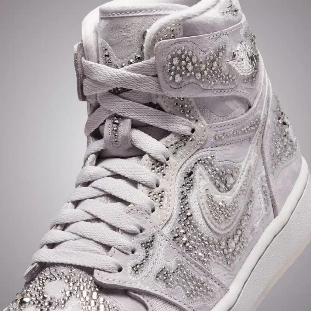 A Swarovski x Air Jordan 1 sneaker adorned with intricate silver rhinestones and detailed embroidery on a light-colored fabric.