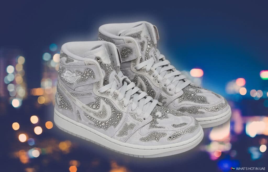 White high-top sneakers adorned with sparkling rhinestones against a blurry city lights backdrop.