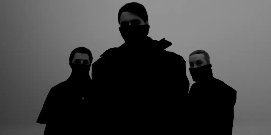 Swedish House Mafia dressed in dark clothing with masks cover their faces, silhouetted against a gray background.