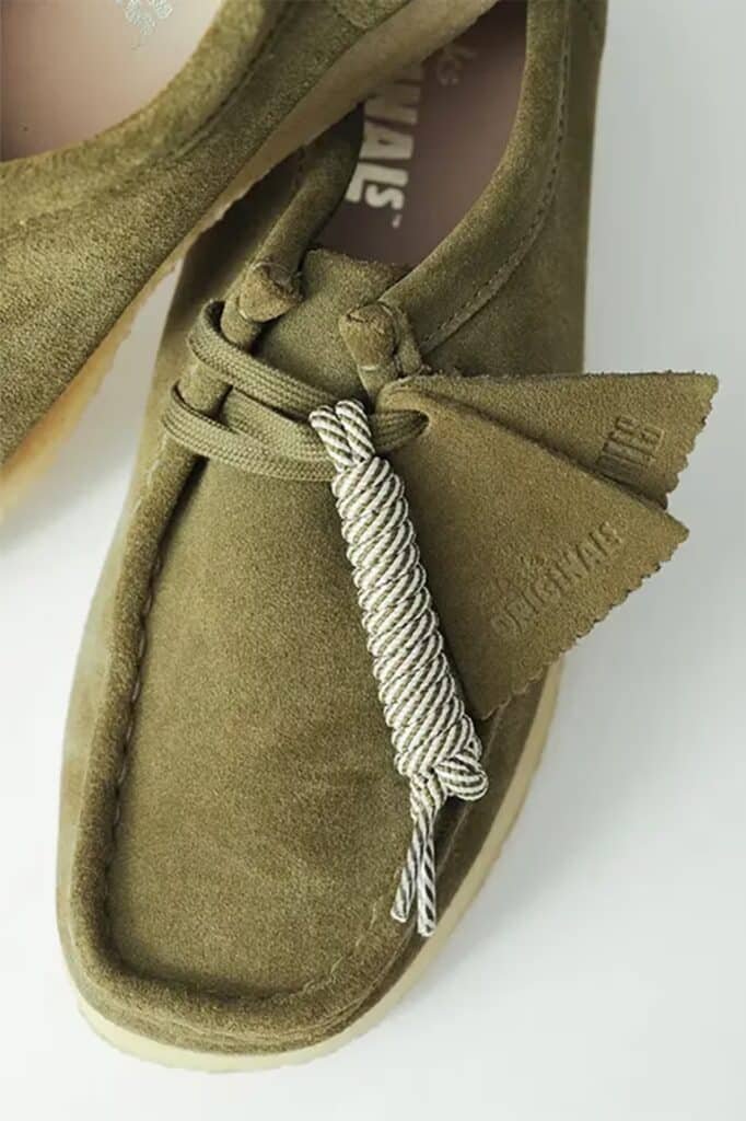 Pair of olive green Urban Research x Clarks Wallabee suede shoes with white cord laces and visible branding on tags.