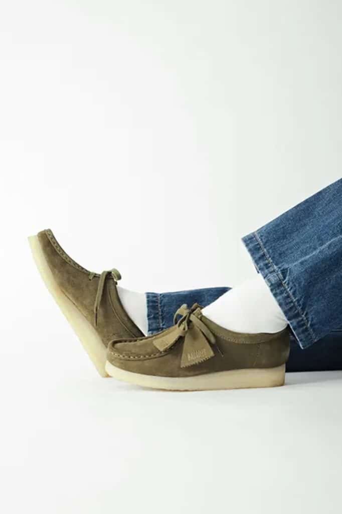 Person wearing olive green Urban Research x Clarks Wallabee suede loafers with tassels and blue jeans.