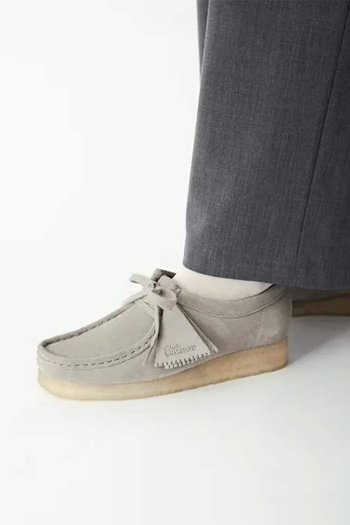 Light grey suede moccasin-style shoe with a crepe sole, worn with dark grey trousers.