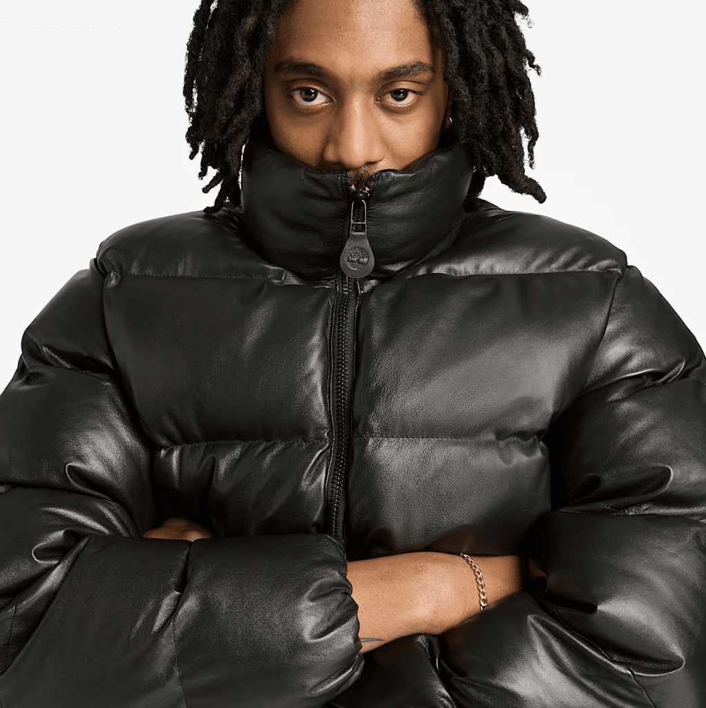 A person with crossed arms wearing a black Timberland Welch Mountain Leather Puffer, looking directly at the camera.