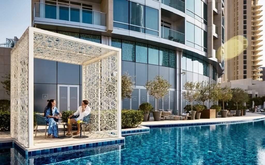 Two people sit at a table in a decorative Address Hotel Dubai Mall outdoor gazebo by a sleek pool outside a modern high-rise building.