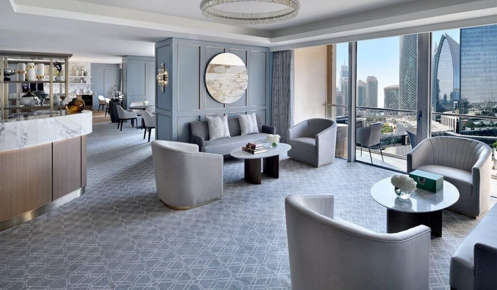 A modern hotel room with elegant grey furniture, cityscape views, and a large mirror on a blue wall.