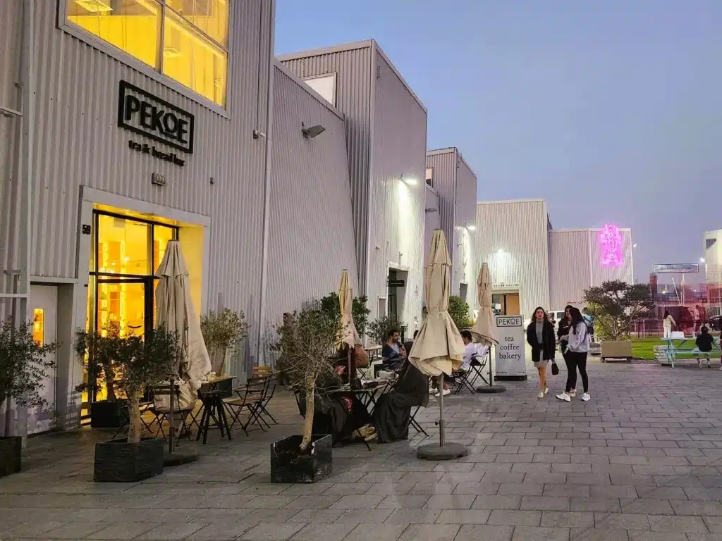 The Best Free Things Worth Doing in the UAE: Outdoor seating area of a café with tables, chairs, and umbrellas, near a lit entrance; people are walking nearby at dusk.