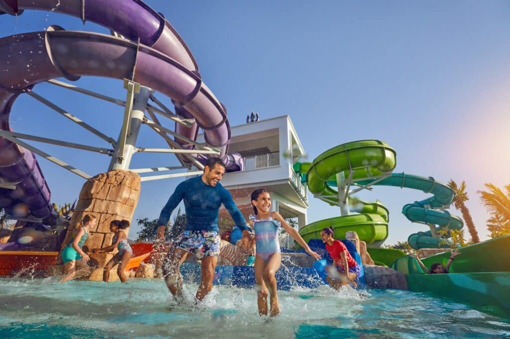 A man and a child in swimwear enjoying a water park with slides and other people around.