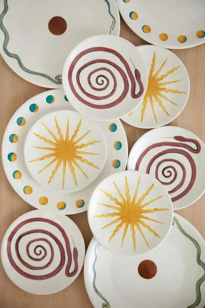A collection of ceramic plates with spiral, sunburst, snake, and dot designs in red, yellow, and green.
