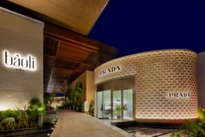 Exterior view of Bâoli Dubai and Prada stores at night, with modern architecture and illuminated signs.