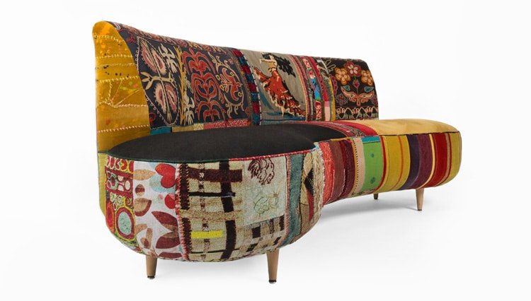A colorful patchwork sofa with a variety of patterns and textures, featuring wooden legs and a modern design.