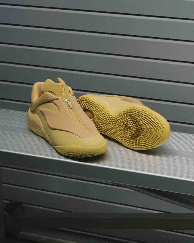 A pair of tan Converse SHAI 001 sneakers with distinctive zip closure and textured yellow soles displayed on a metallic surface.