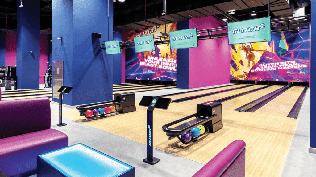 A modern bowling alley with vibrant colors, digital screens, and bowling balls lined up on racks.