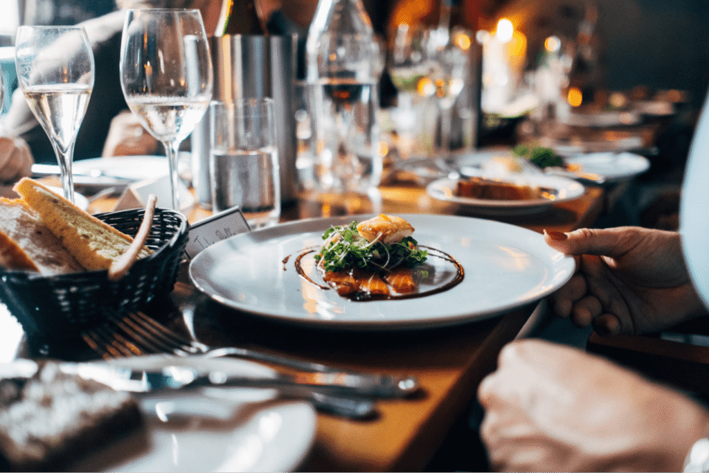 A gourmet dish with greens and sauce is served on a plate at a sophisticated dining setting with glasses and bread.