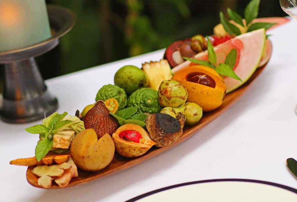 Fine Dining in Dubai, A wooden platter with assorted tropical fruits, including lychee, papaya, and pineapple, arranged on a white tablecloth.